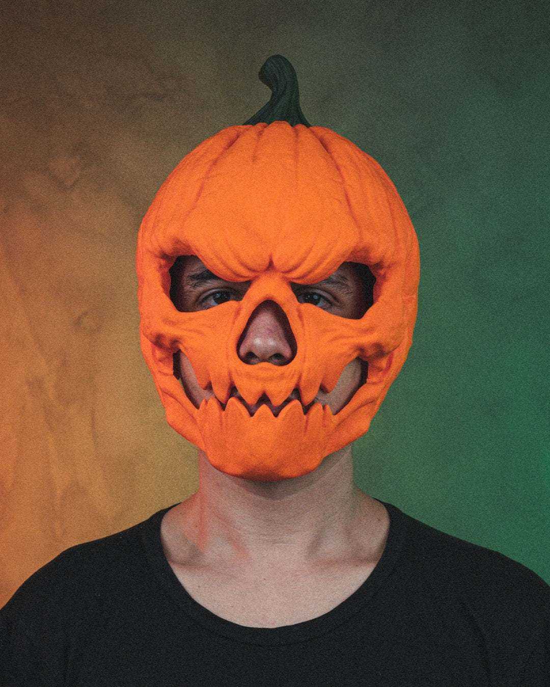 Pumpkin Head Mask in bright orange with a dark green stem, carved eye openings and a jagged toothy grin